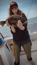 Angler proudly displaying a Flounder while fishing on a boat, showcasing a successful catch in a coastal environment.