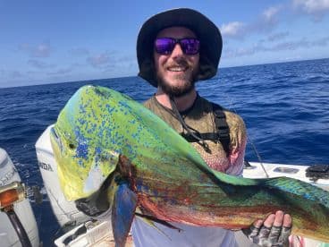 An angler proudly displaying a vibrant Mahi Mahi while fishing offshore, showcasing the beautiful blue ocean backdrop.