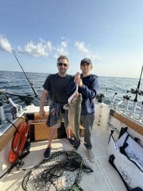 A young angler and an adult proudly displaying a large Walleye on a fishing boat, showcasing their successful catch during a day on the water.