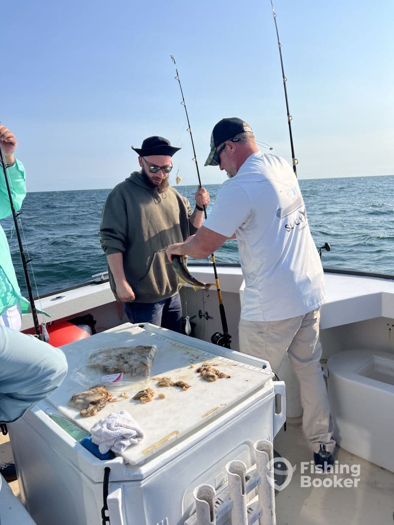 Two anglers engaged in fishing on a boat, with one preparing to reel in a catch while the other observes. The scene captures the excitement of fishing in open waters.