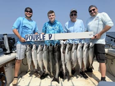 A group of anglers proudly displaying their catch of salmon on a catch board while out on the water.