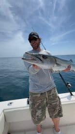 Angler proudly displaying a large Barracuda while fishing offshore, showcasing a sunny day on the water.