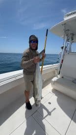 Angler proudly displaying a large fish aboard a fishing boat in clear waters, showcasing a successful day on the water.