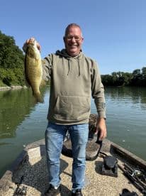 An adult angler proudly displaying a large Largemouth Bass while fishing on a calm river, showcasing a beautiful day on the water.