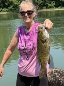 An angler proudly displaying a large Smallmouth Bass while fishing on a serene river.