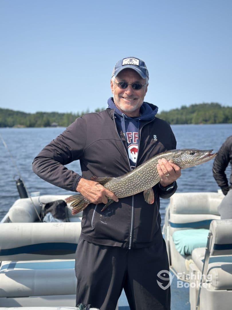 An adult angler proudly displaying a Northern Pike while fishing on a serene lake, showcasing a successful catch during a relaxing day on the water.