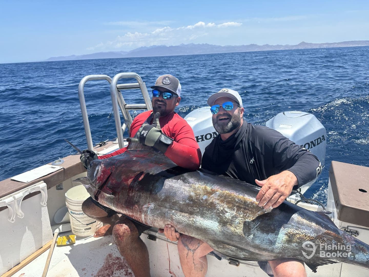 Two anglers proudly displaying a large Bluefin Tuna aboard a fishing boat in open waters, showcasing their successful catch during a deep-sea fishing trip.