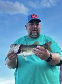 An angler proudly displaying a large Largemouth Bass against a clear blue sky, showcasing a successful day of fishing.