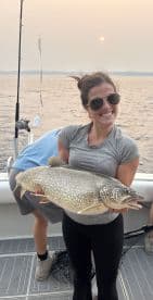 A proud angler displaying a large Lake Trout while fishing on a boat during sunset.