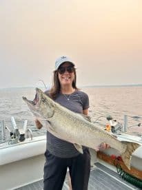An angler proudly displaying a large Chinook Salmon while fishing on a boat, showcasing a successful day on the water.