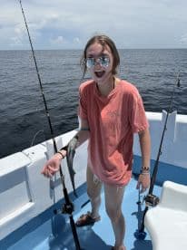 A young angler excitedly holding a small shark while fishing on a boat, showcasing the thrill of the catch in open waters.