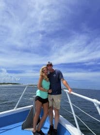 A couple enjoying a sunny day on the deck of a fishing boat, with a scenic view of the water and sky.