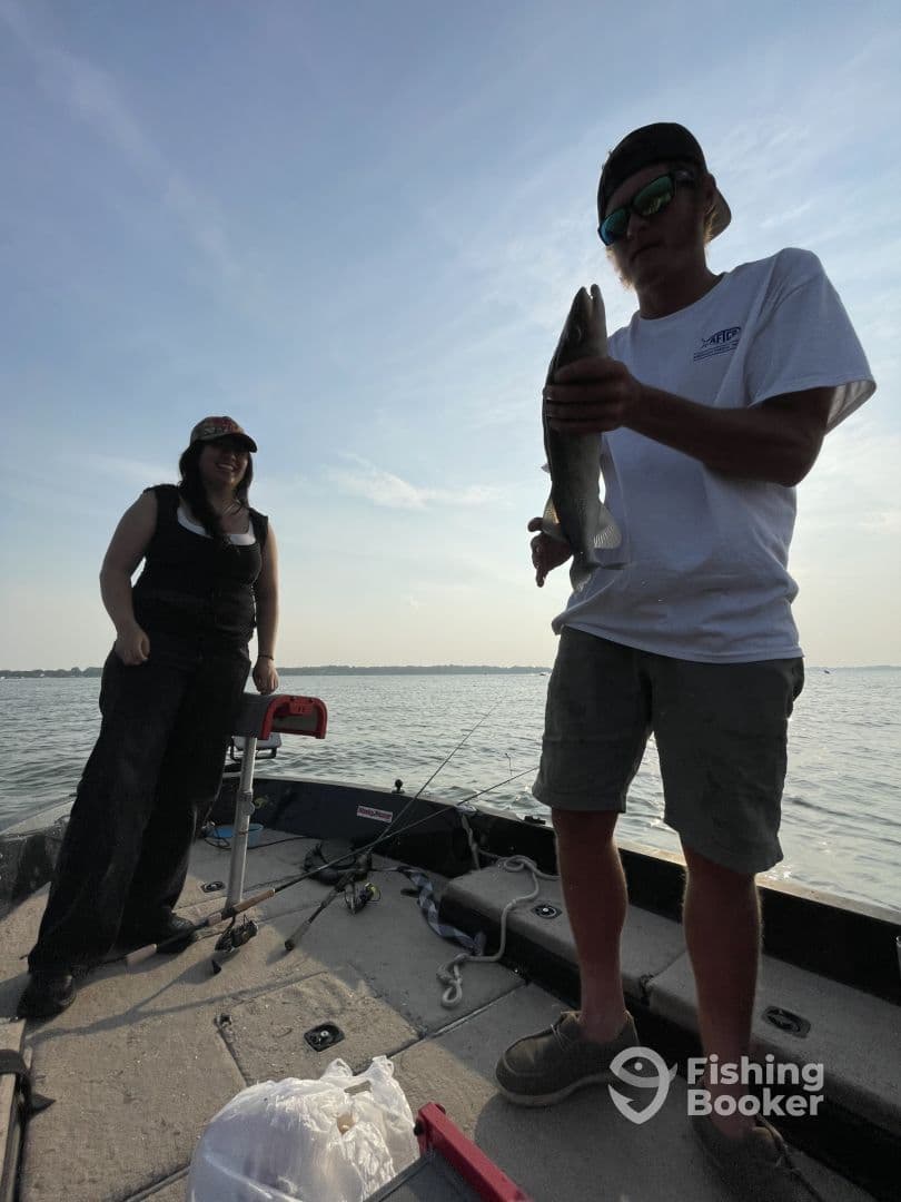 Two anglers enjoying a sunny day on the water, with one proudly displaying a caught fish on a fishing boat.