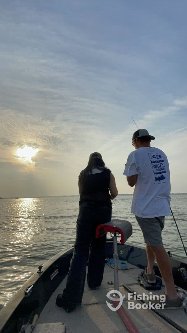 Two anglers engaged in fishing on a small boat during sunset, creating a serene atmosphere on the water.