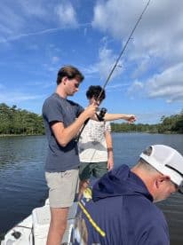 Two young anglers actively fishing on a boat in a scenic waterway, showcasing the excitement of a fishing adventure.