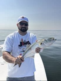 Angler holding a large Speckled Trout while fishing on a calm day in a coastal waterway.