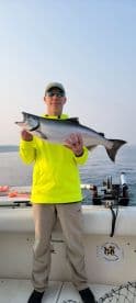 Angler proudly displaying a large Salmon while fishing on a charter boat in a serene lake environment.