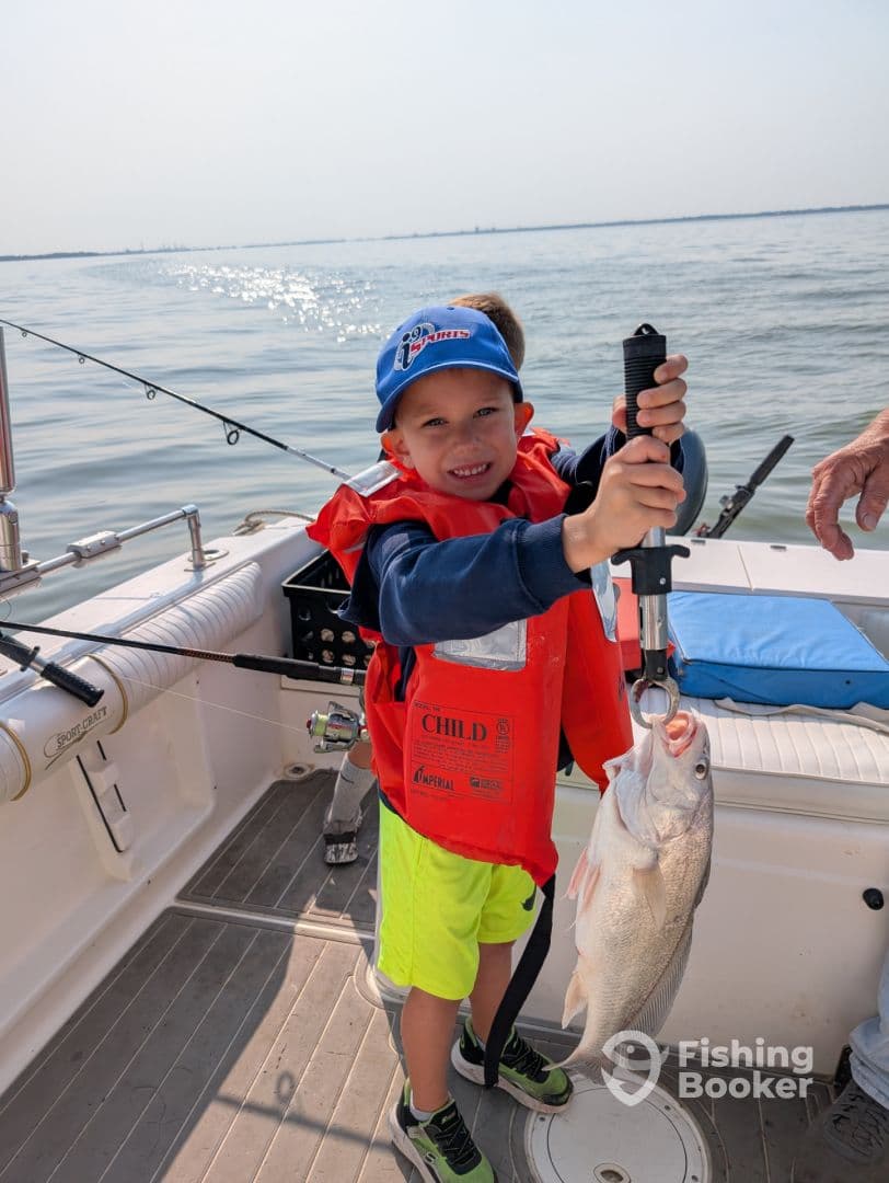 A young angler in a life jacket proudly displaying a large fish while fishing on a boat, showcasing a fun family fishing experience.