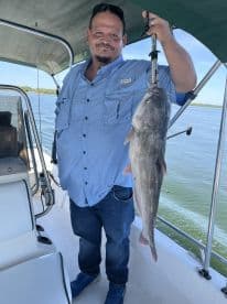 An angler proudly displaying a large Catfish while aboard a boat, showcasing a successful fishing trip.