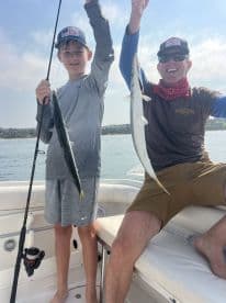A young angler and an adult proudly displaying their catch of two fish while on a boat, enjoying a day of fishing.