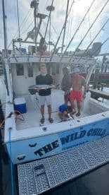 A young angler proudly displaying a large fish on the deck of 'The Wild Child' charter boat, surrounded by family members after a successful fishing trip.