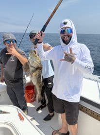 A group of anglers celebrating a successful catch of a large grouper while fishing offshore, showcasing camaraderie and excitement.