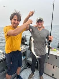 A young angler and an adult proudly displaying a caught fish while fishing on a boat, showcasing a successful day on the water.