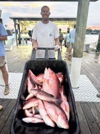 A smiling angler stands with a cart full of freshly caught Red Snapper at the dock, showcasing a successful fishing trip.