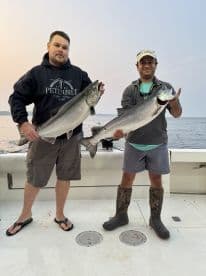 Two anglers proudly displaying their catch of Chinook Salmon while fishing on a boat, showcasing a successful day on the water.