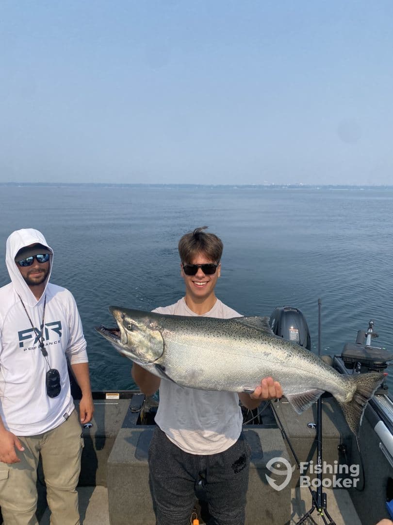A young angler proudly displays a large Salmon while fishing on a boat, showcasing a successful day on the water.
