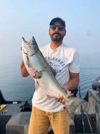An angler proudly displaying a large Salmon while fishing on a calm lake, showcasing a successful day on the water.