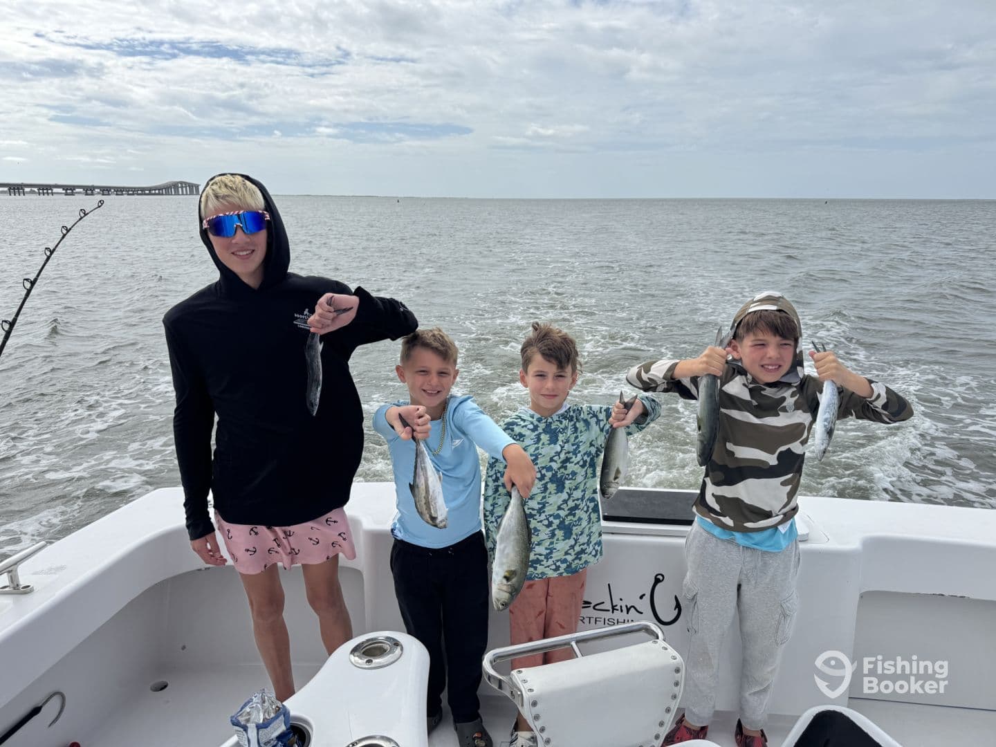 Four young anglers proudly displaying their catch of speckled trout while enjoying a fishing trip on a boat.