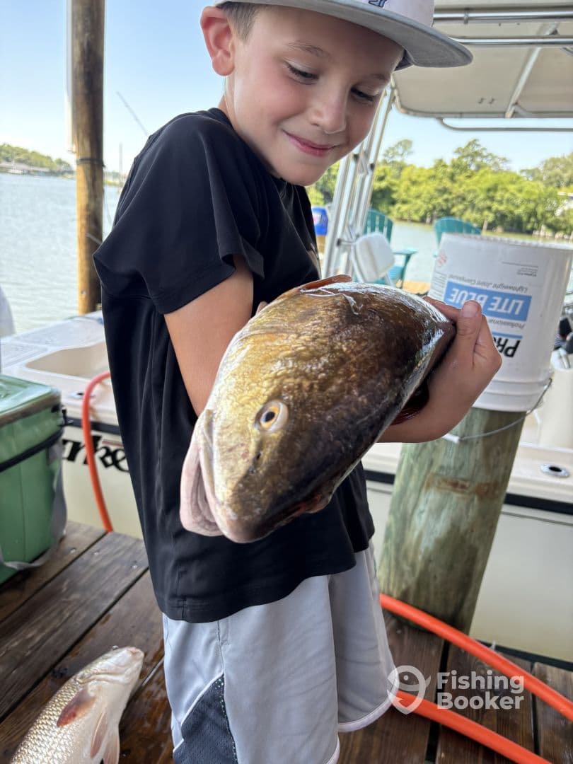 A young angler joyfully holding a large fish at the dock, showcasing a successful fishing trip.