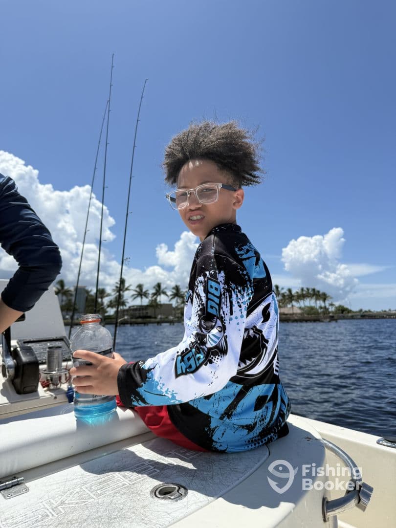 A young angler enjoying a day on the boat, holding a drink while fishing in a sunny coastal environment.
