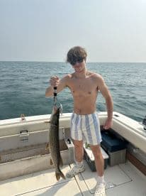 A young angler proudly displaying a Northern Pike while fishing on a boat, showcasing a sunny day on the water.