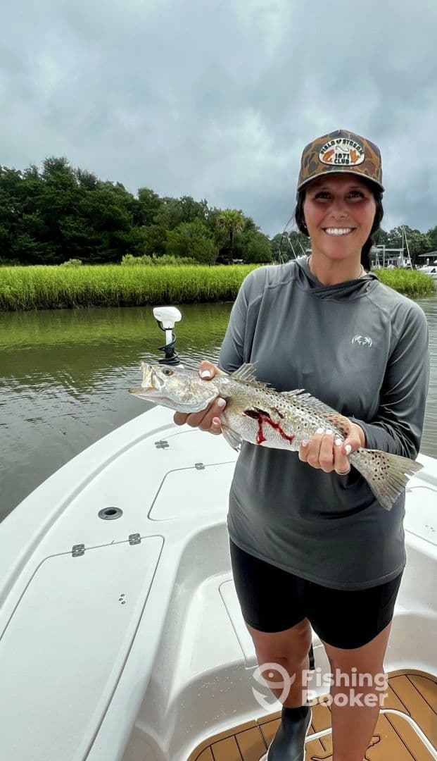 Angler proudly displaying a Speckled Trout while fishing in a scenic coastal environment.