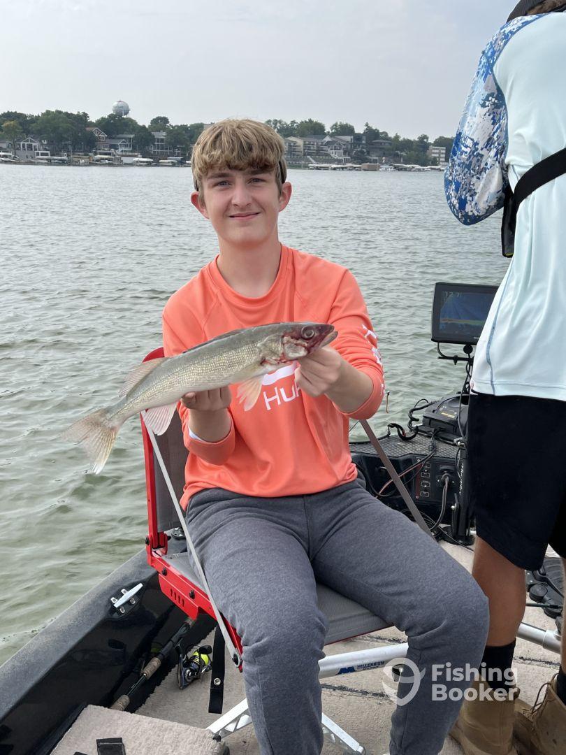 A young angler proudly displaying a Walleye while fishing from a boat on a calm lake, showcasing a successful day on the water.