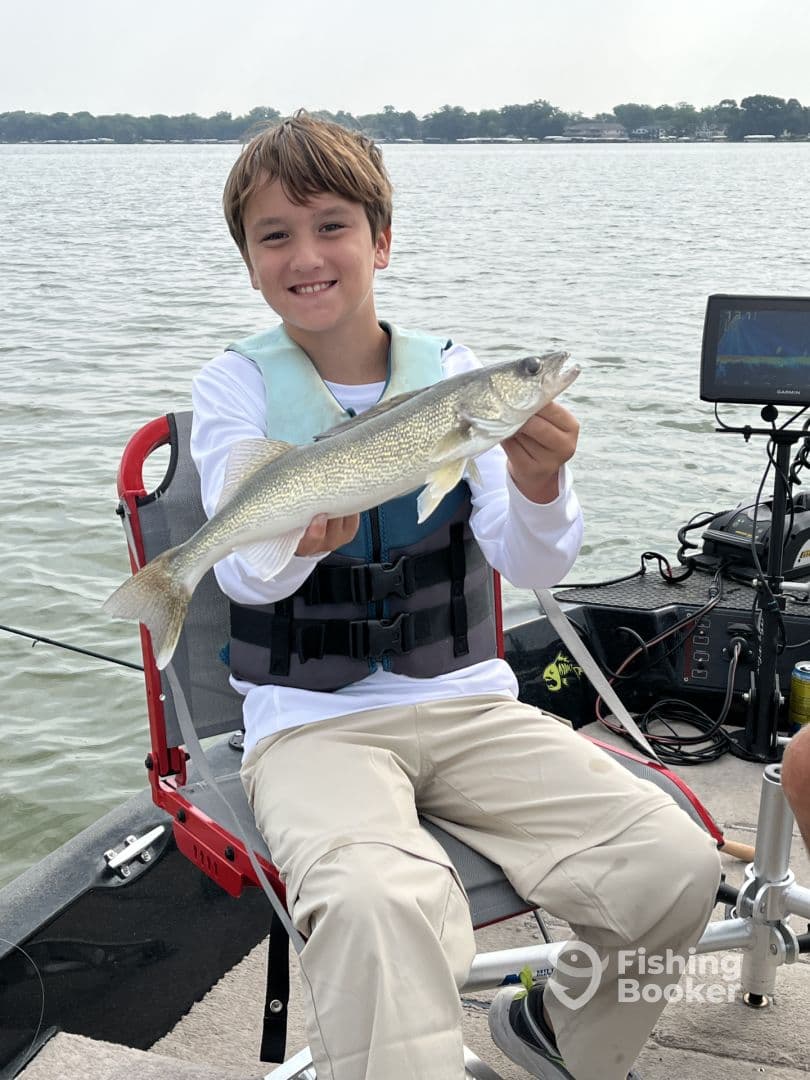 A young angler proudly displaying a Walleye while seated on a fishing boat, showcasing a successful day on the water.