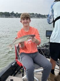 A young angler proudly displaying a Walleye while fishing from a boat on a calm lake, showcasing a successful day on the water.