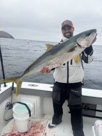 Angler proudly displaying a large Yellowtail while fishing offshore, showcasing a successful day on the water.