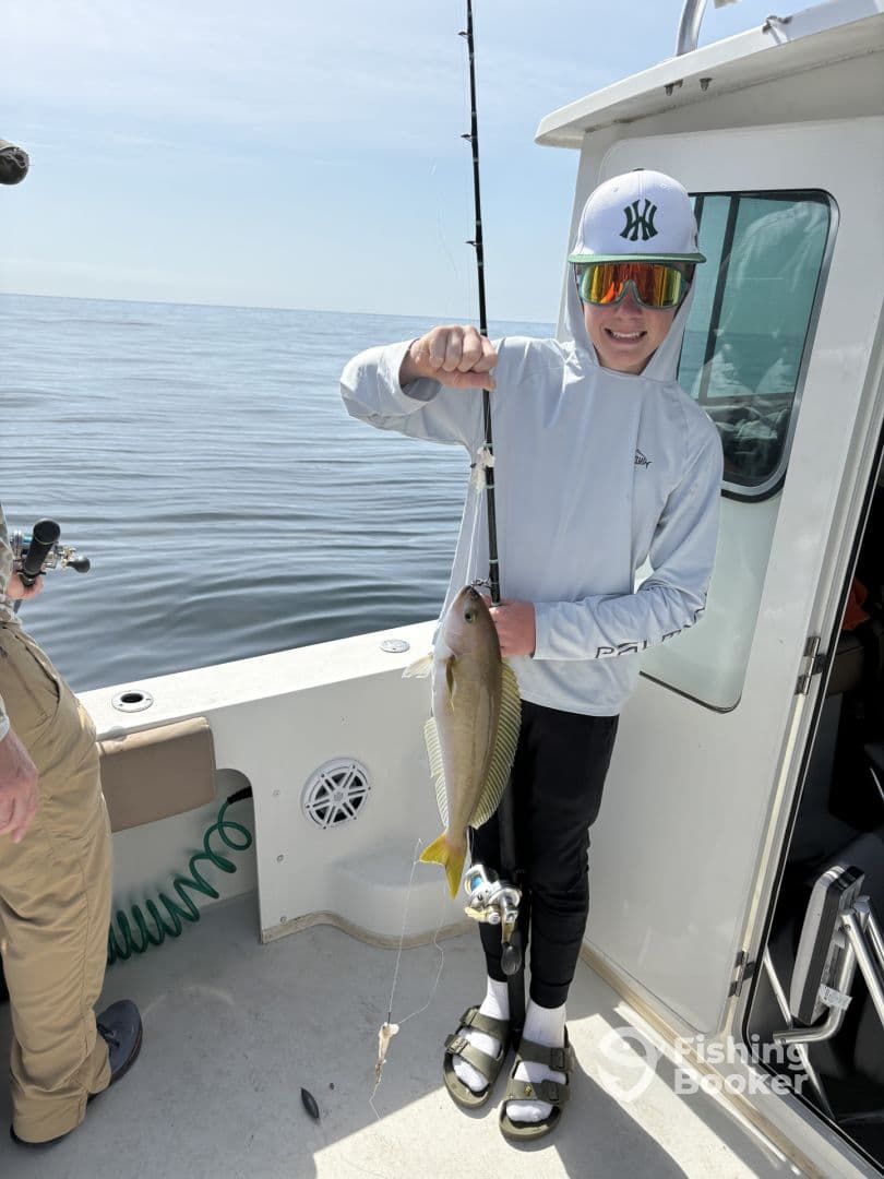 A young angler proudly displaying a freshly caught fish while fishing on a boat, showcasing a sunny day on the water.