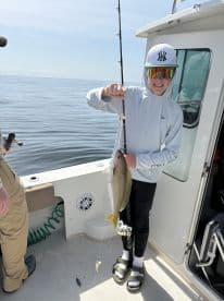 A young angler proudly displaying a freshly caught fish while fishing on a boat, showcasing a sunny day on the water.