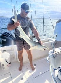 An angler proudly displaying a large shark aboard a fishing boat, showcasing a successful day on the water.