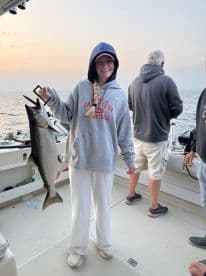 A young angler proudly displaying a large fish on a boat during a fishing trip, with a scenic ocean backdrop.