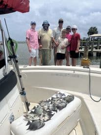 A family group poses with their catch of various fish on a cooler aboard a boat, showcasing a successful fishing trip.