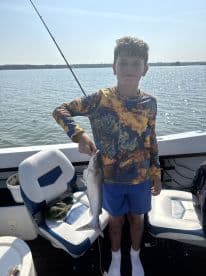 A young angler proudly displaying a caught catfish while fishing on a boat, enjoying a sunny day on the water.