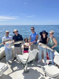 A family group proudly displaying their catch of striped bass while enjoying a sunny day on the water.