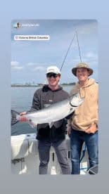 Two anglers proudly displaying a large Salmon caught during a fishing trip in Victoria, British Columbia.