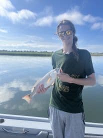 A young angler proudly displaying a Redfish while fishing on calm waters, showcasing a beautiful day on the water.