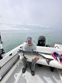 Angler displaying a large Salmon on a fishing boat, showcasing a successful catch during a serene day on the water.